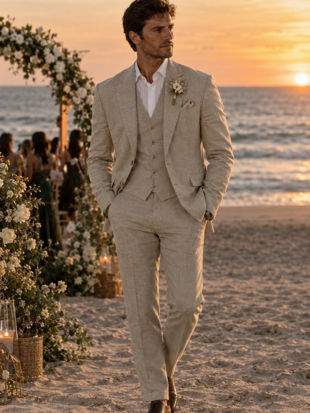 Man in a beige linen three-piece suit standing on a beach at sunset.