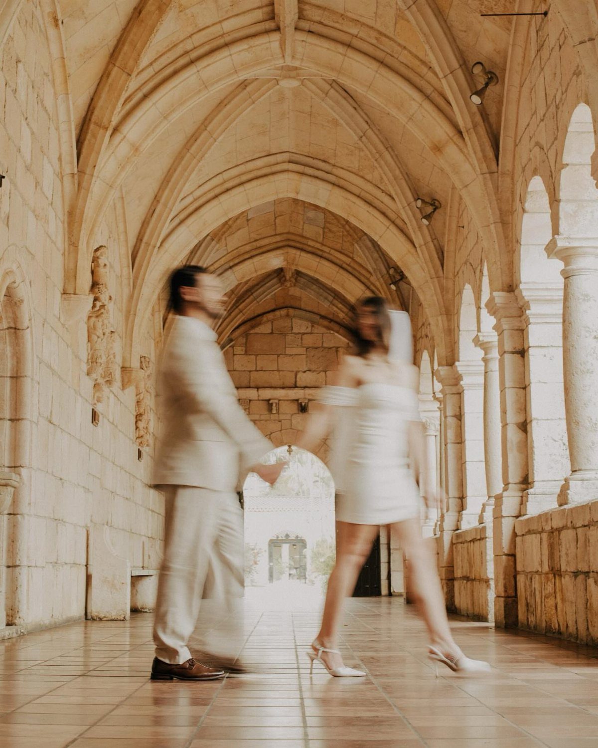 Couple in formal wear walking through ancient stone Gothic arches and corridors.
