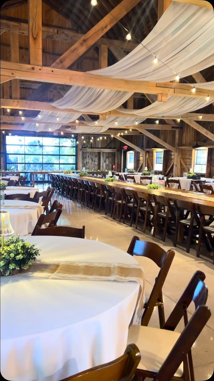 Rustic barn wedding venue with white fabric ceiling draping and long wooden tables.
