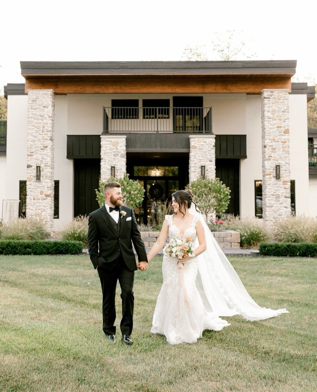 Bride and groom walking on a lawn in front of a modern estate venue.