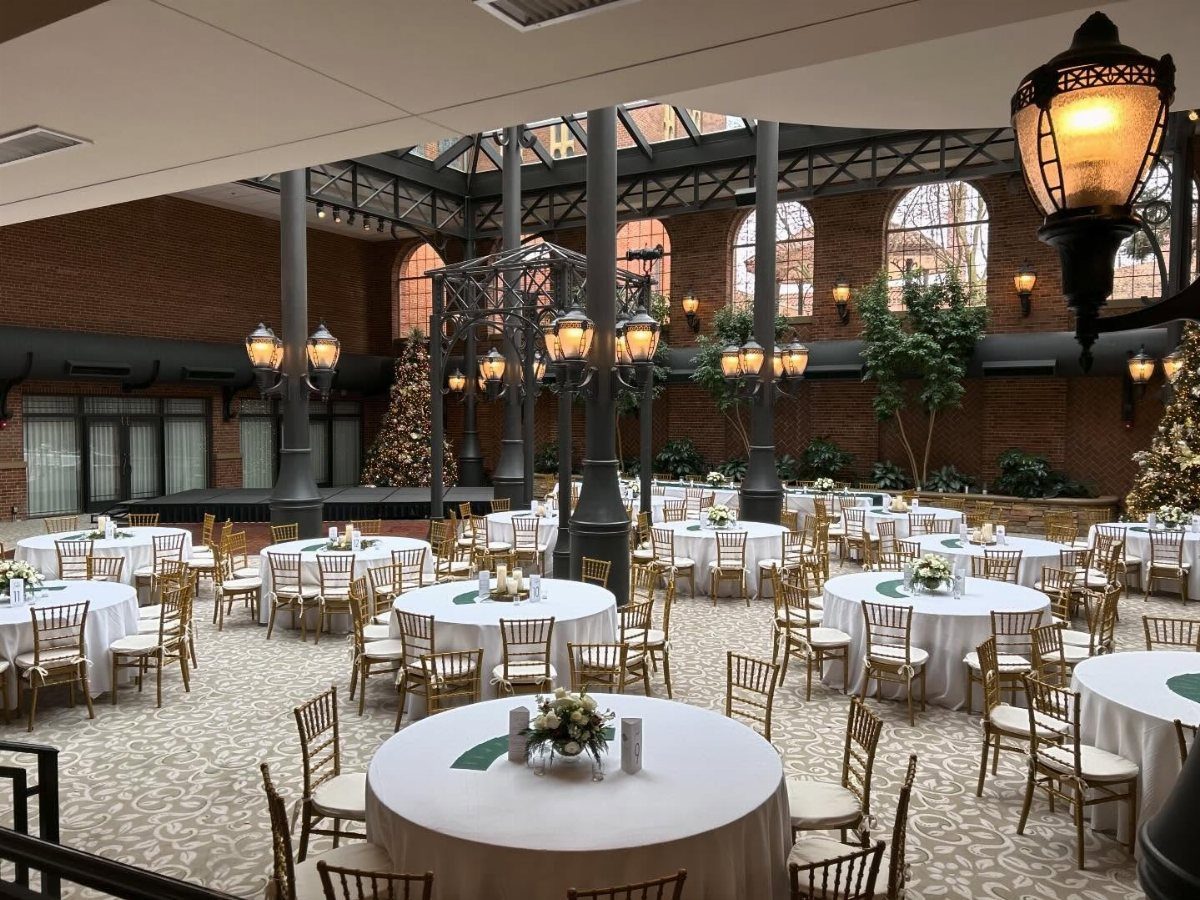 Indoor wedding reception space with round tables, gold chairs, and a glass ceiling.