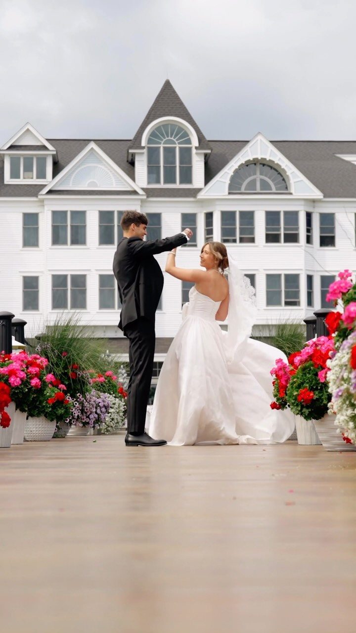 Bride and groom dancing on a wooden deck before a large white estate building.