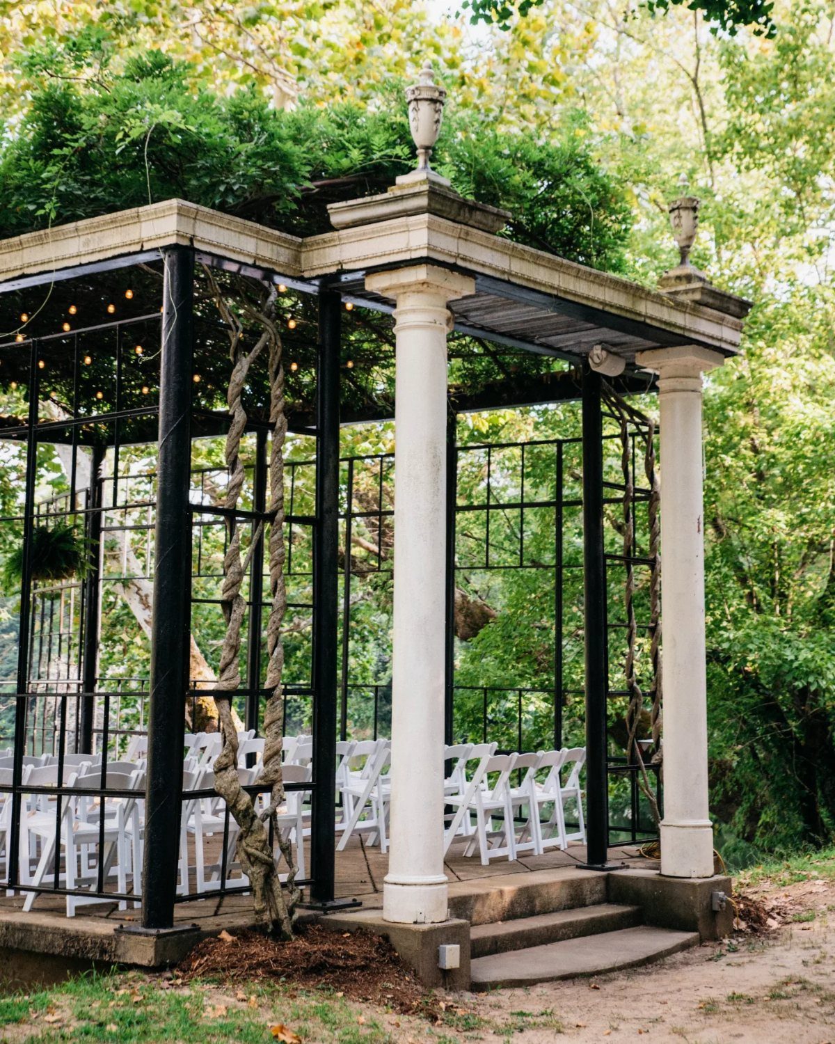 White classical gazebo with columns and white chairs set in a lush green garden