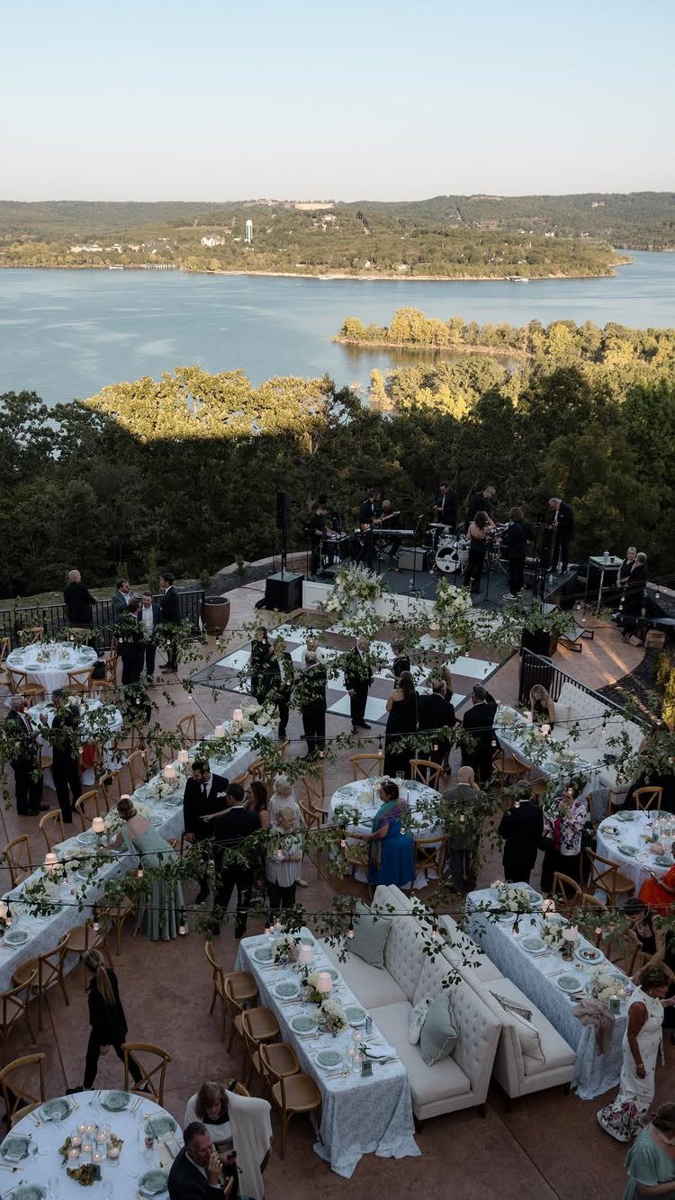 Outdoor wedding reception terrace with white tables overlooking a scenic lake and hills.
