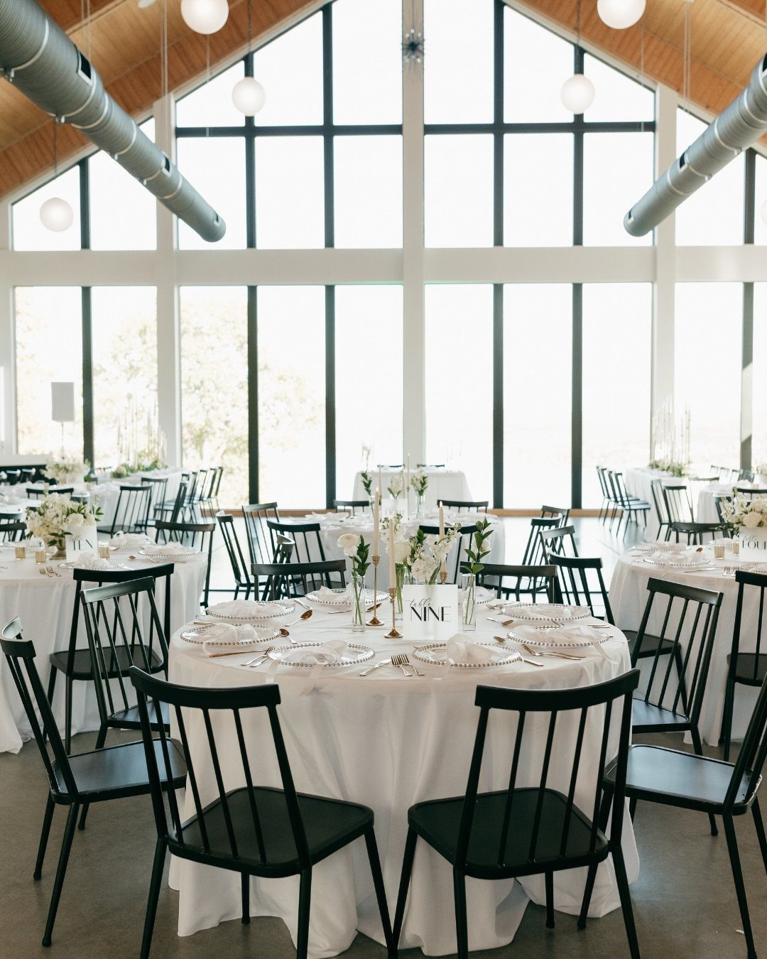 Modern event space with round tables, black chairs, and large floor-to-ceiling windows.