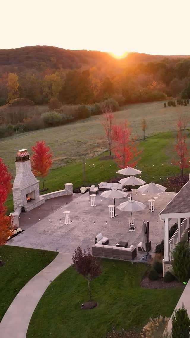 Outdoor stone patio with fireplace and umbrellas overlooking autumn hills at sunset.