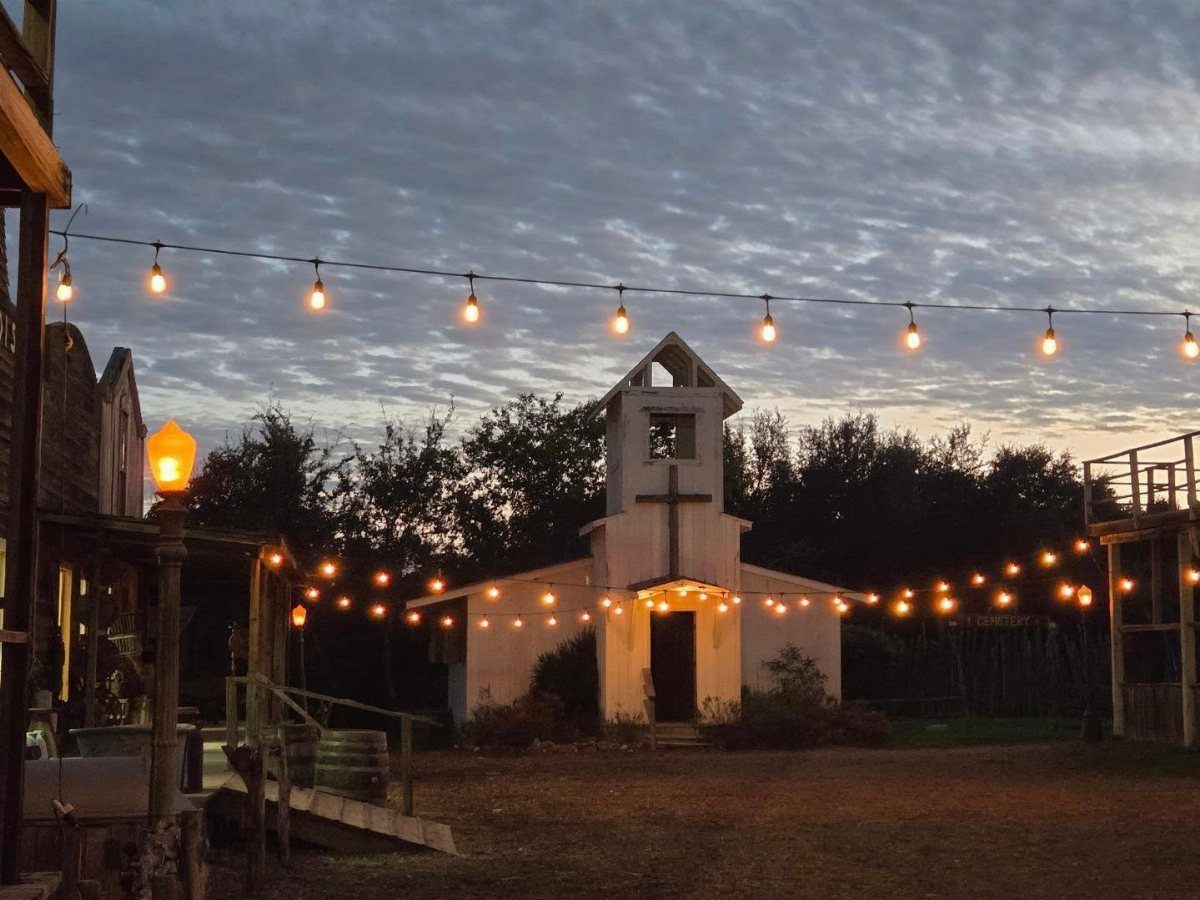 Small white wooden chapel with a steeple and string lights at dusk.