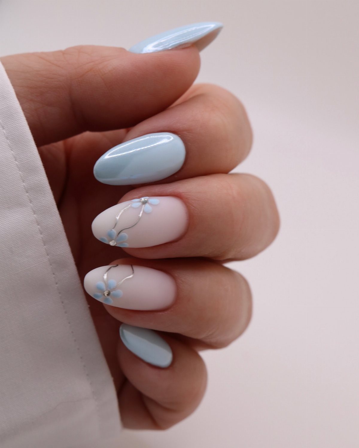 Almond shaped nails with light blue polish and milky white floral accents.