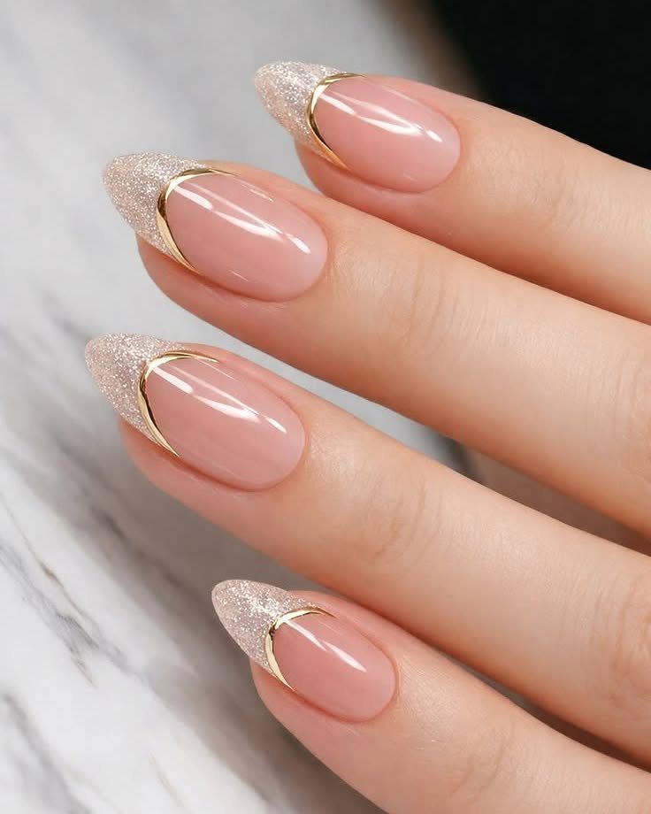 Almond nails with nude base and shimmering champagne gold glitter tips on marble.