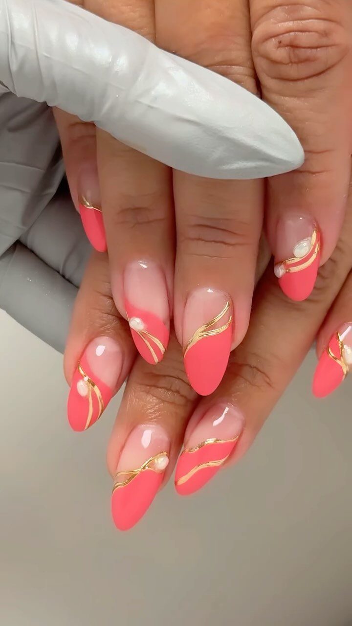 Coral almond-shaped nails with gold curved lines and small white pearl accents.