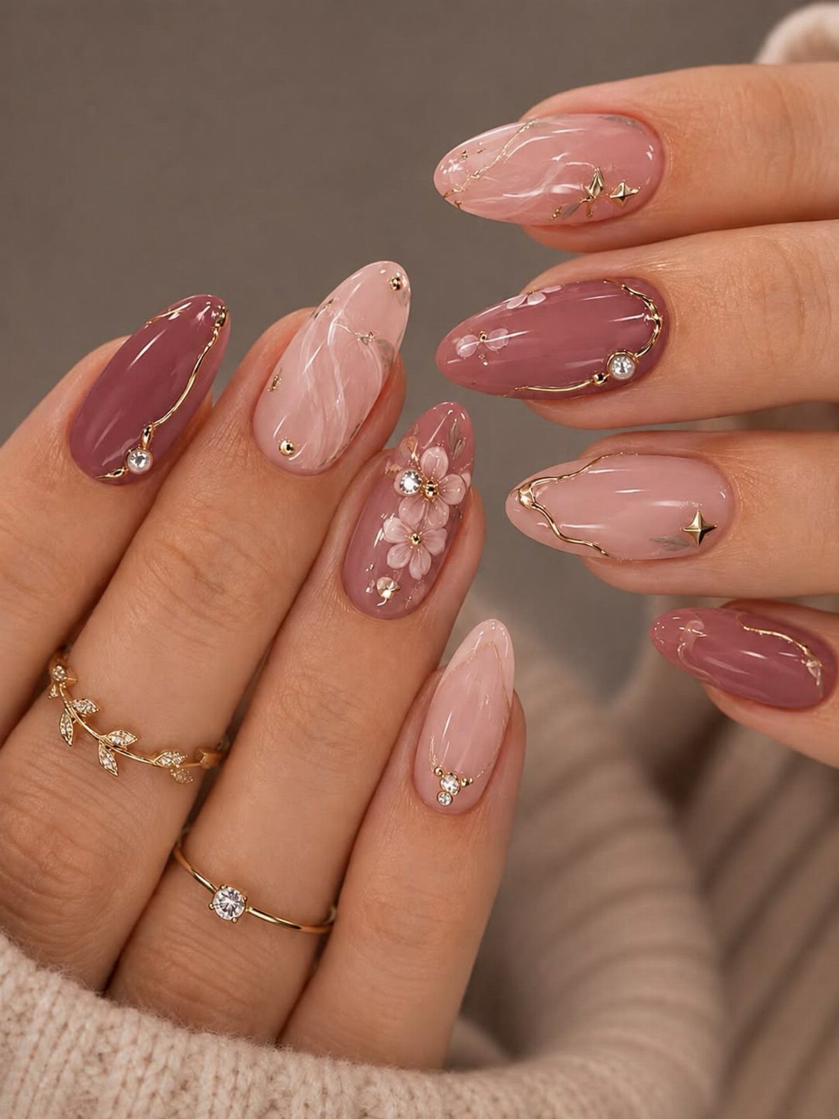 Almond shaped nails with mauve and pink polish, gold swirls, and 3D white flowers.