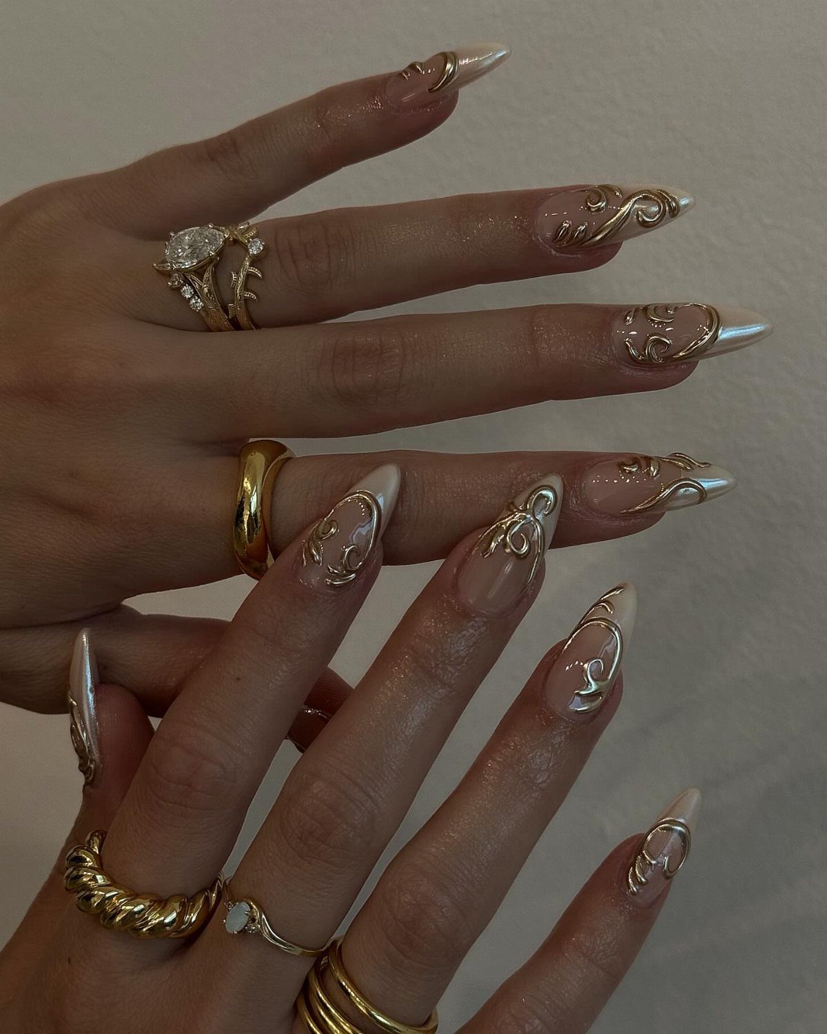 Nude almond nails with gold swirl designs and gold wedding rings on fingers.