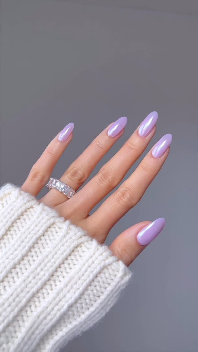 Lavender chrome almond nails on a hand wearing a diamond ring and white sweater.