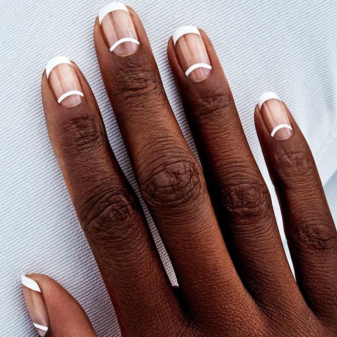Almond shaped nails with white tips and crescent lines on dark skin.