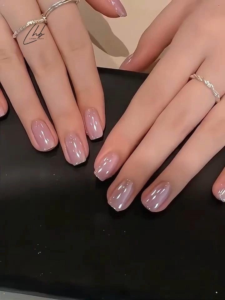 Nude almond-shaped nails with a glossy finish on hands wearing silver rings.