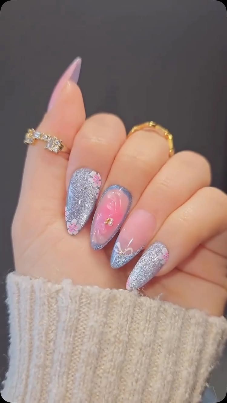 Almond nails with blue glitter, pink ombre, and floral accents on a hand.