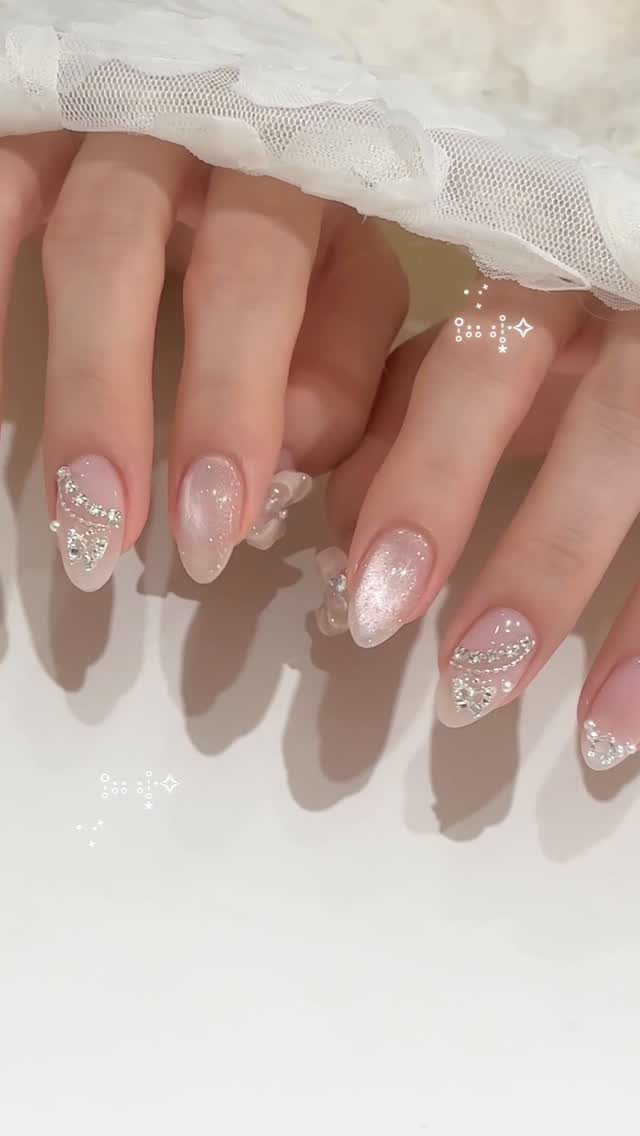 Pearlescent white almond-shaped nails with silver rhinestones and glittery swirls on hands.
