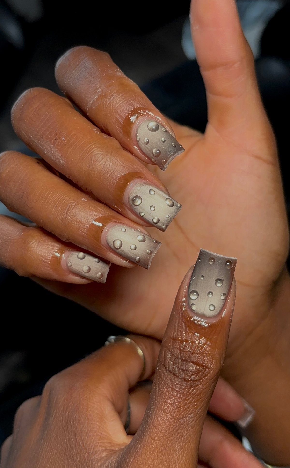 Taupe square nails with clear 3D raised water droplet accents on a hand.