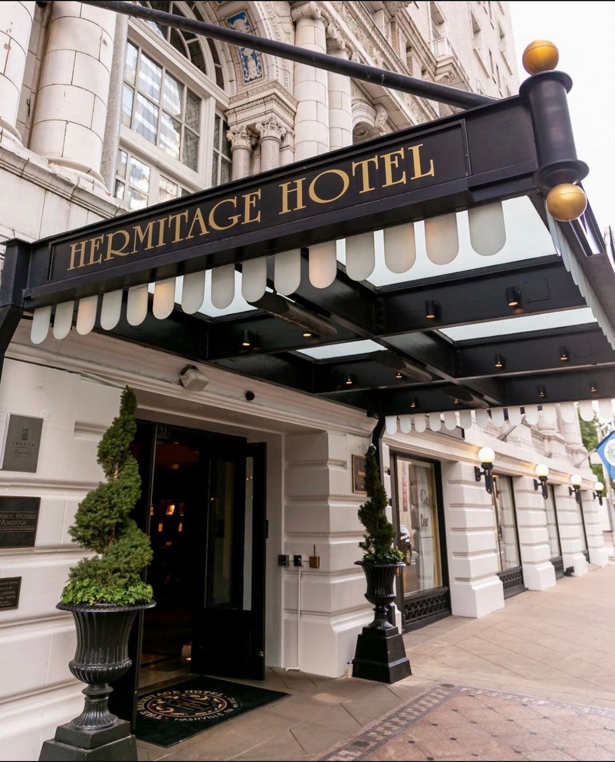 The Hermitage Hotel entrance with a black and gold canopy and spiral topiaries.
