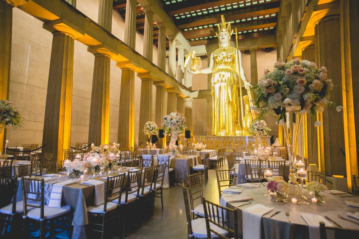 Grand hall with golden Athena statue and elegant wedding reception table settings.
