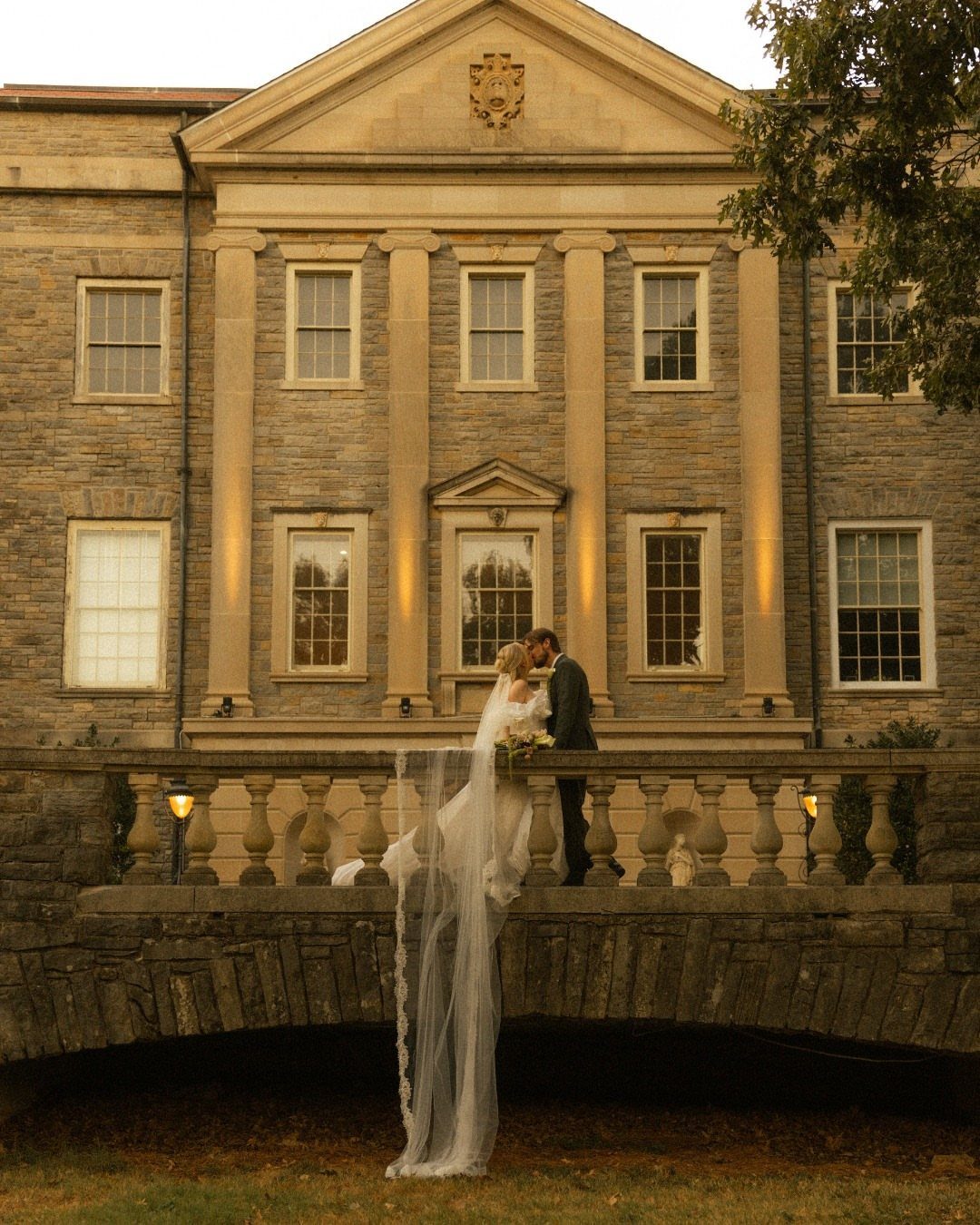 Bride and groom kissing on the stone balcony of a historic mansion.