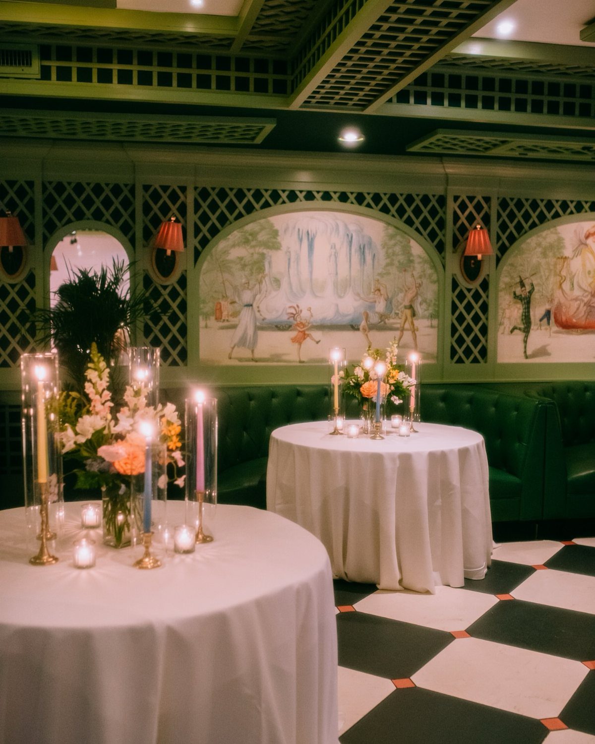 Elegant indoor event space with white clothed tables, candles, and green leather seating.