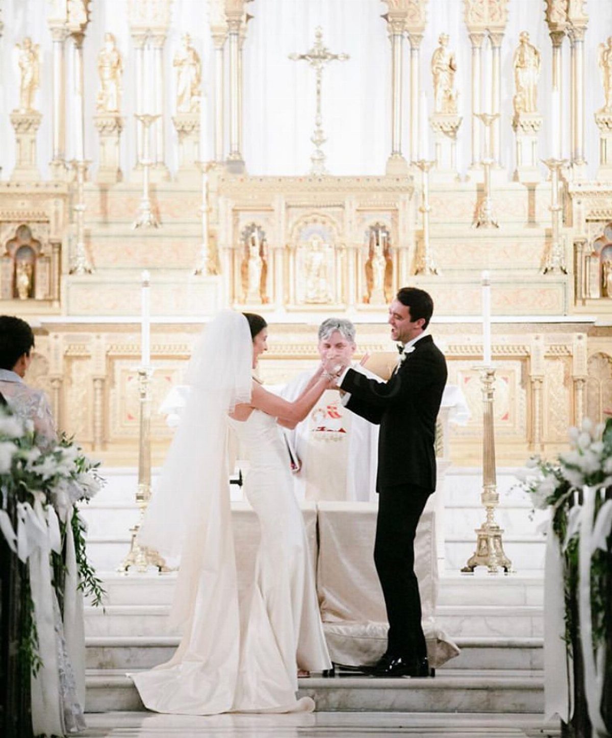 Bride and groom holding hands at a wedding ceremony before a gold church altar.