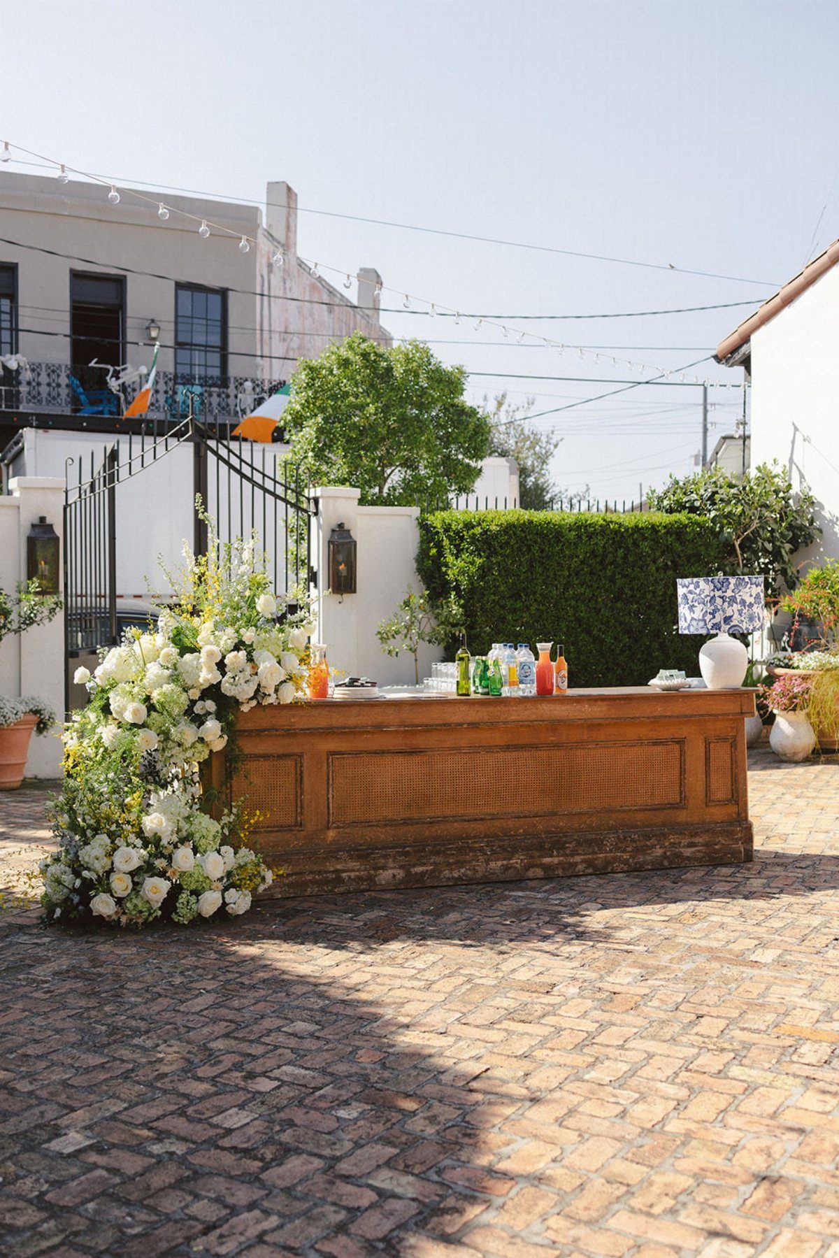Wooden bar with white floral arrangements in a sunny brick courtyard venue.