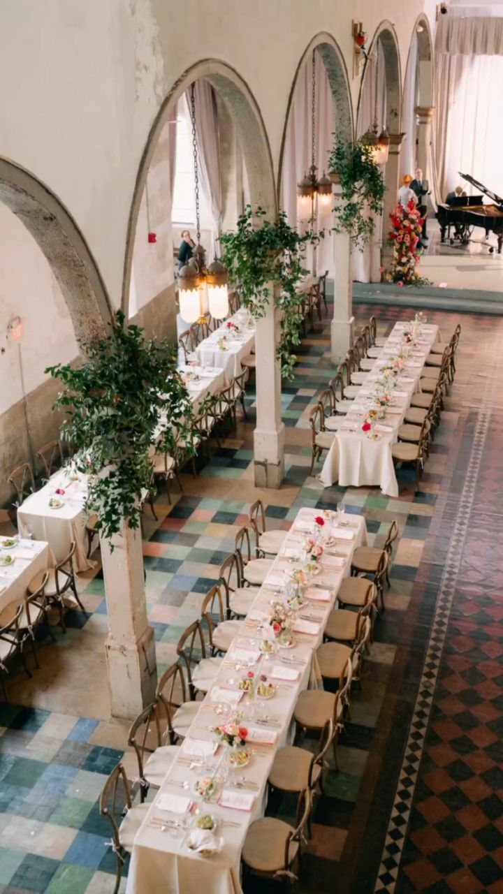 Long banquet tables set for a wedding in a hall with high arches.
