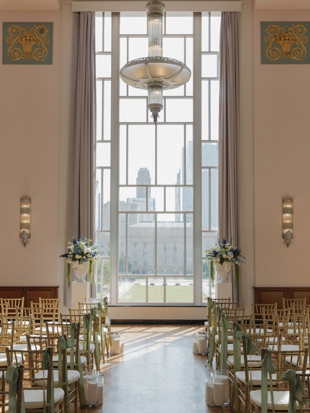 Wedding ceremony setup with gold chairs and Art Deco chandelier in a historic hall.