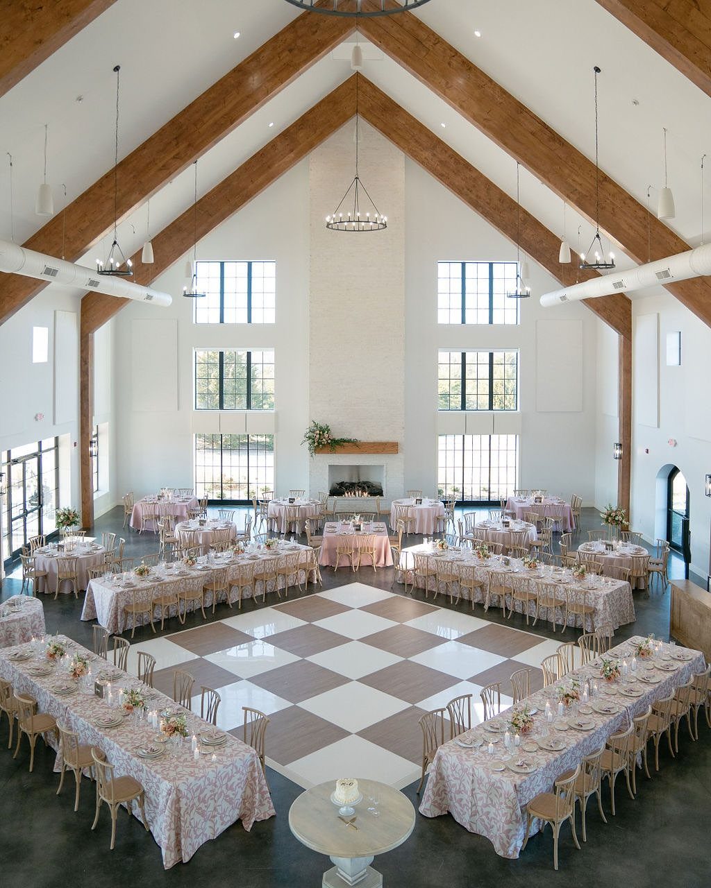 Modern wedding venue interior with wooden beams, checkered dance floor, and decorated tables.