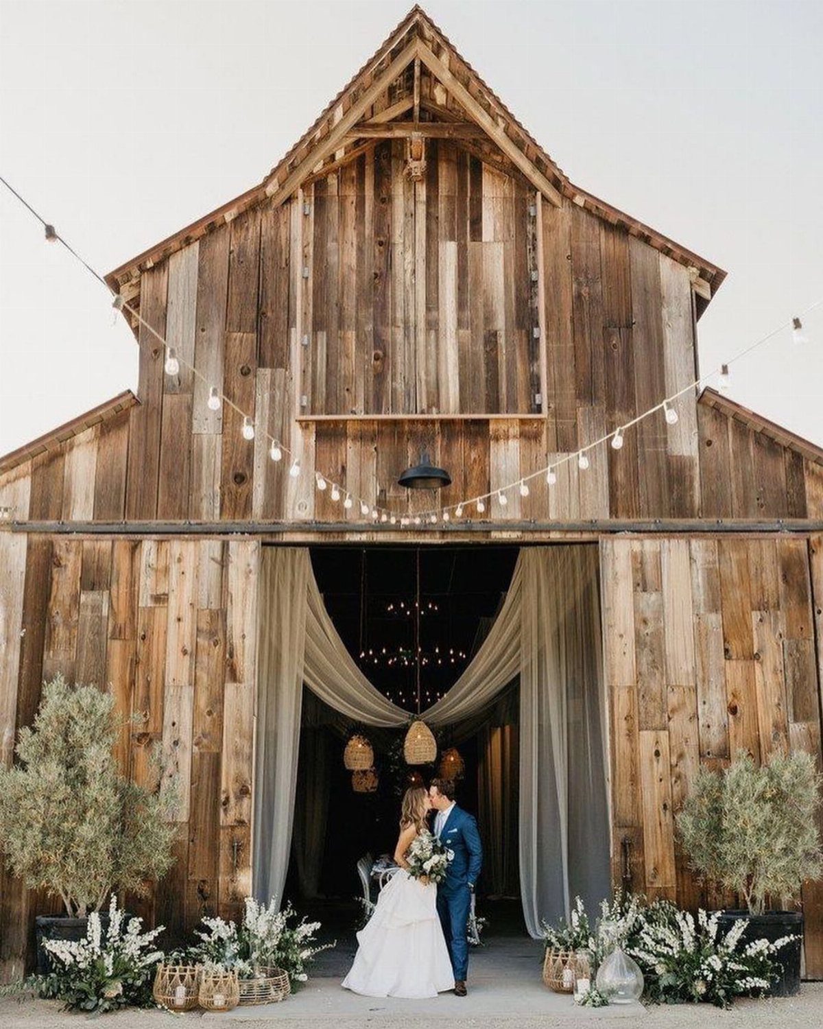 Bride and groom posing in front of a rustic wooden barn wedding venue.