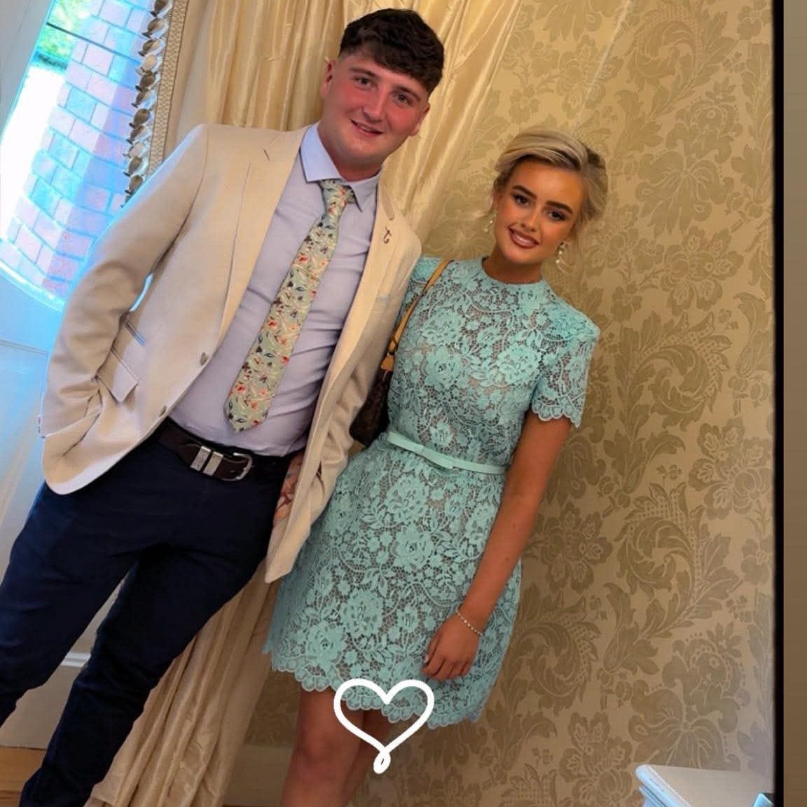 Woman wearing a mint green lace dress posing with a man in a blazer.
