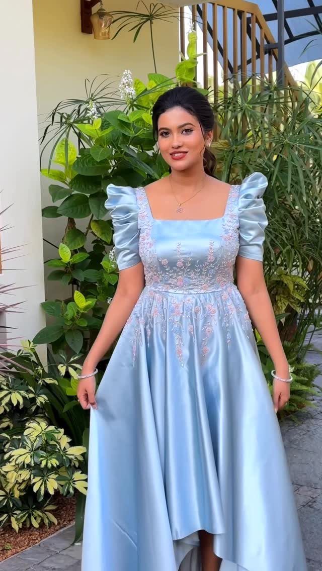 Woman in a light blue satin dress with puff sleeves and floral embroidery.