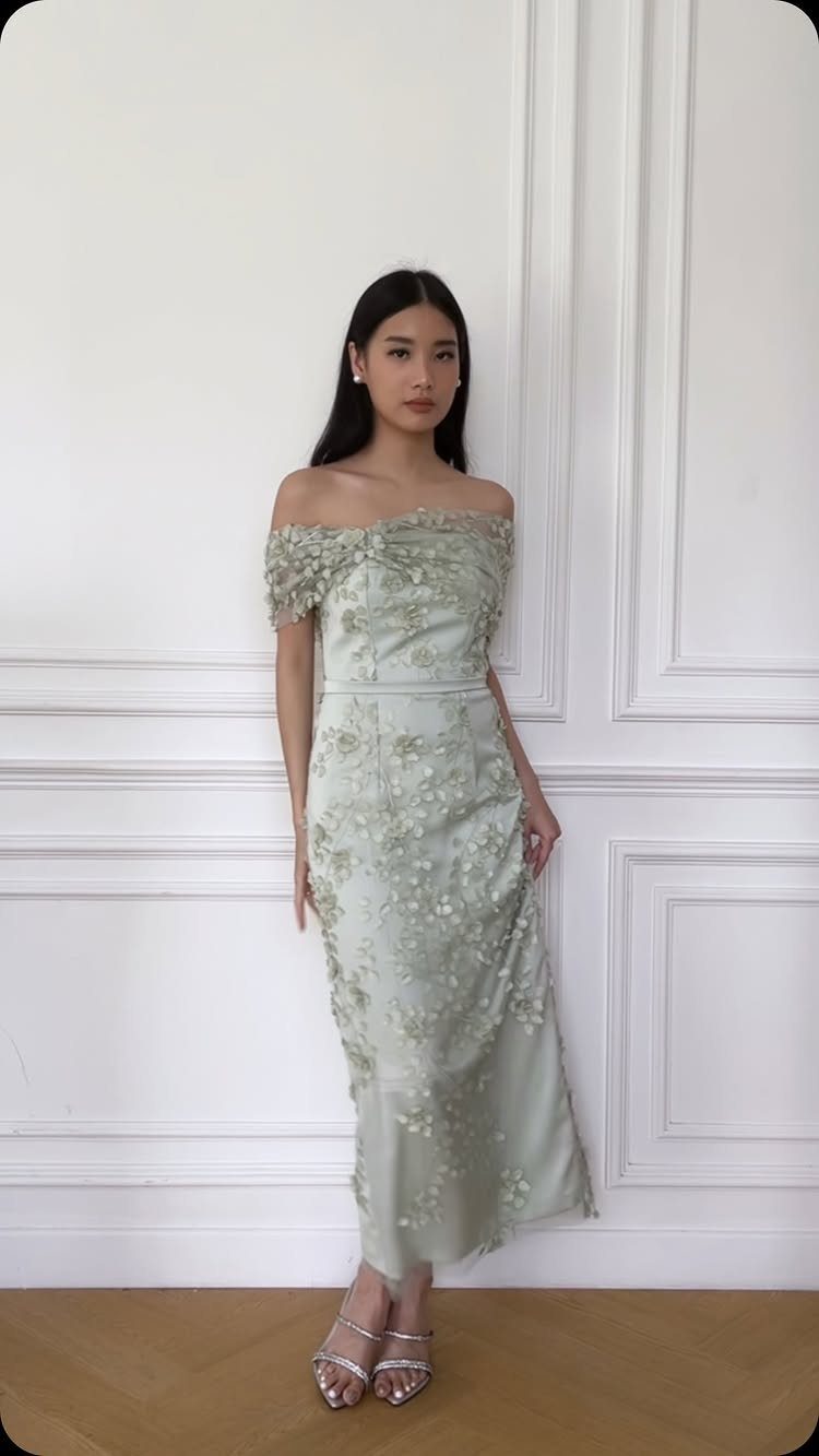 Woman wearing an off-the-shoulder sage green floral embroidered dress and silver heels.