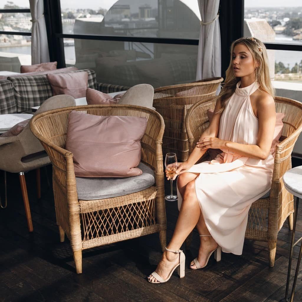 Woman wearing a soft peach midi dress sitting in a wicker chair.