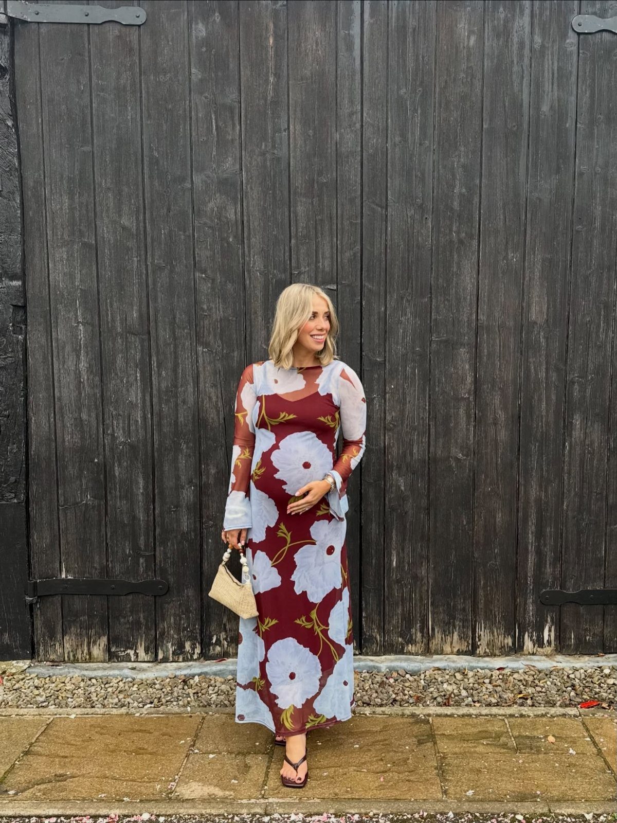 Pregnant woman in a burgundy floral maxi dress posing before dark wooden doors.