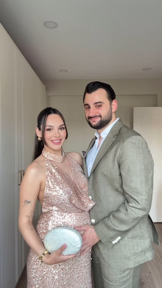 Pregnant woman in a rose-gold sequined dress and man in a green suit posing.