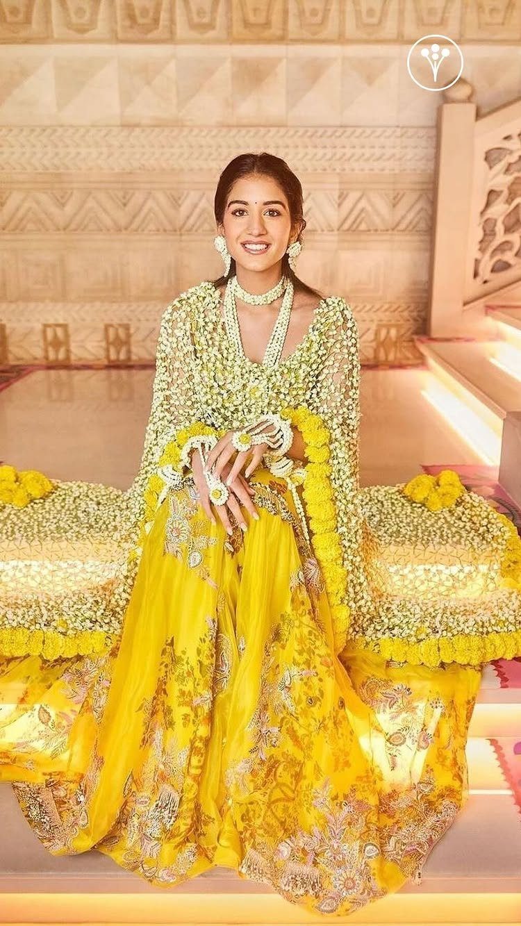 Woman in a bright yellow embroidered lehenga and floral jewelry for a Haldi ceremony.