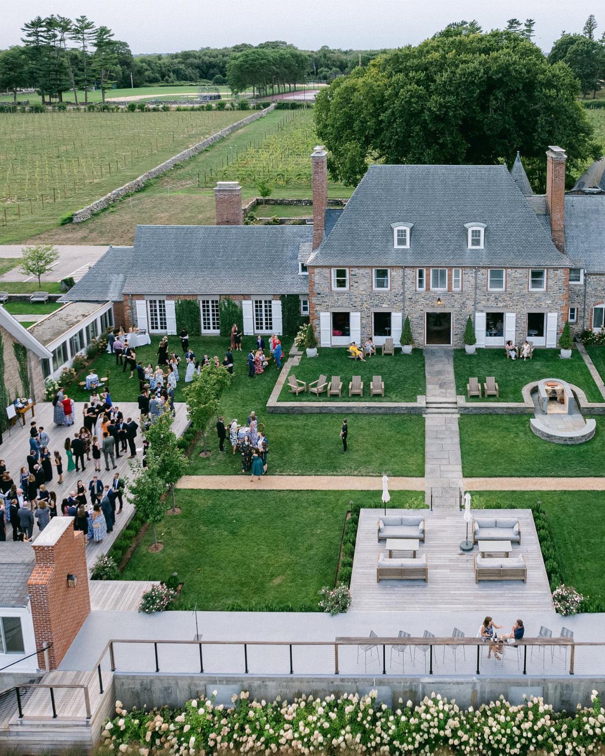 Stone manor house with guests on the lawn and a vineyard in the background
