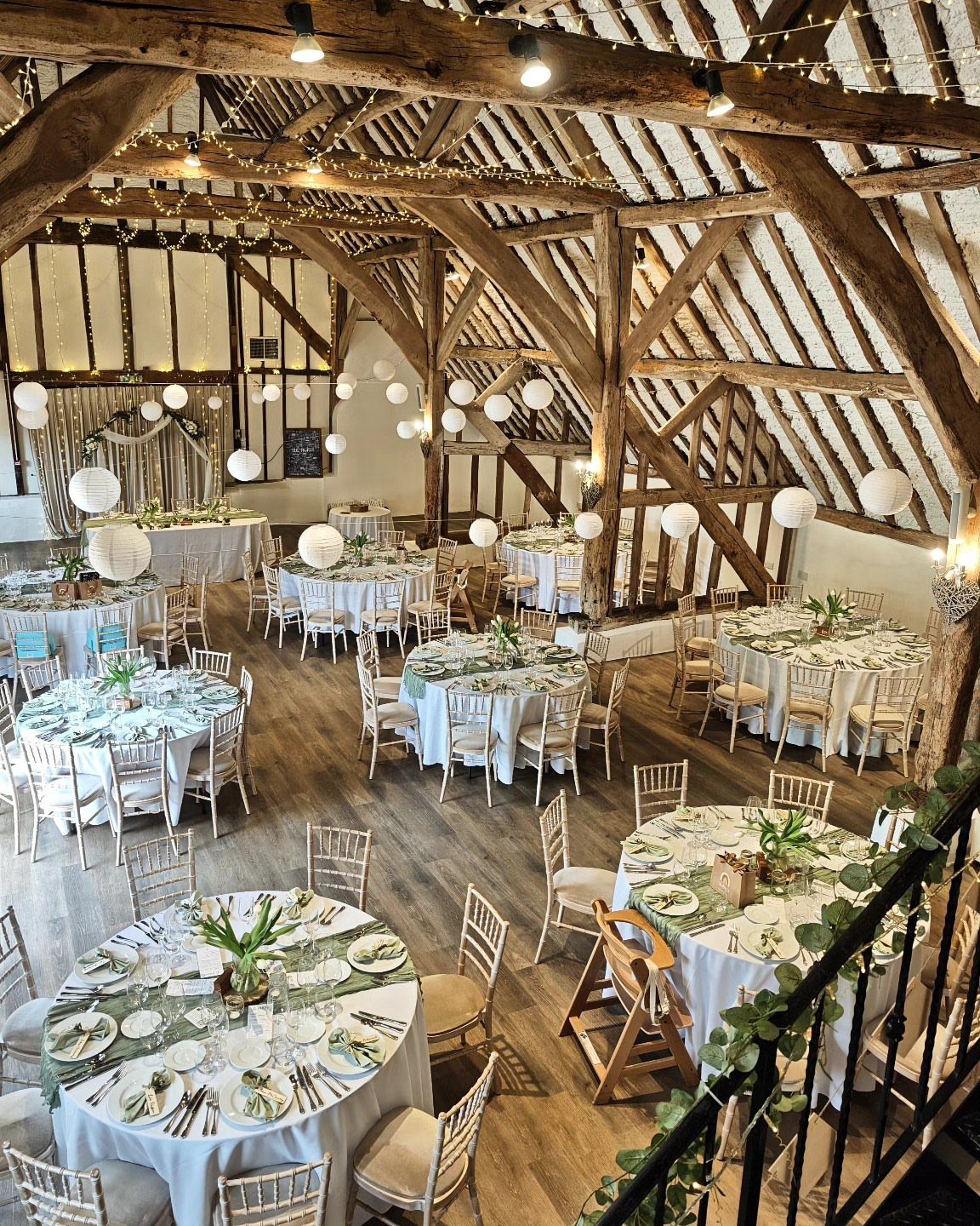 Rustic barn interior with round dining tables, exposed wooden beams, and white lanterns.