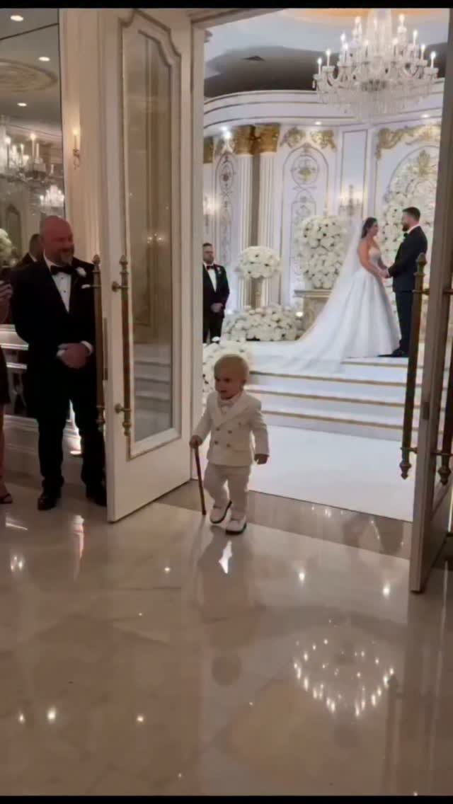Young boy in a white suit and cane at a wedding ceremony.