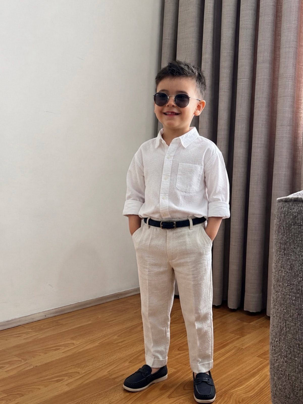 Young boy in a white button-up shirt and white trousers wearing sunglasses.
