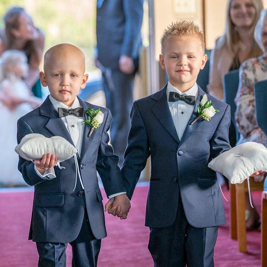 Two young ring bearers in navy blue suits and black bow ties holding pillows.
