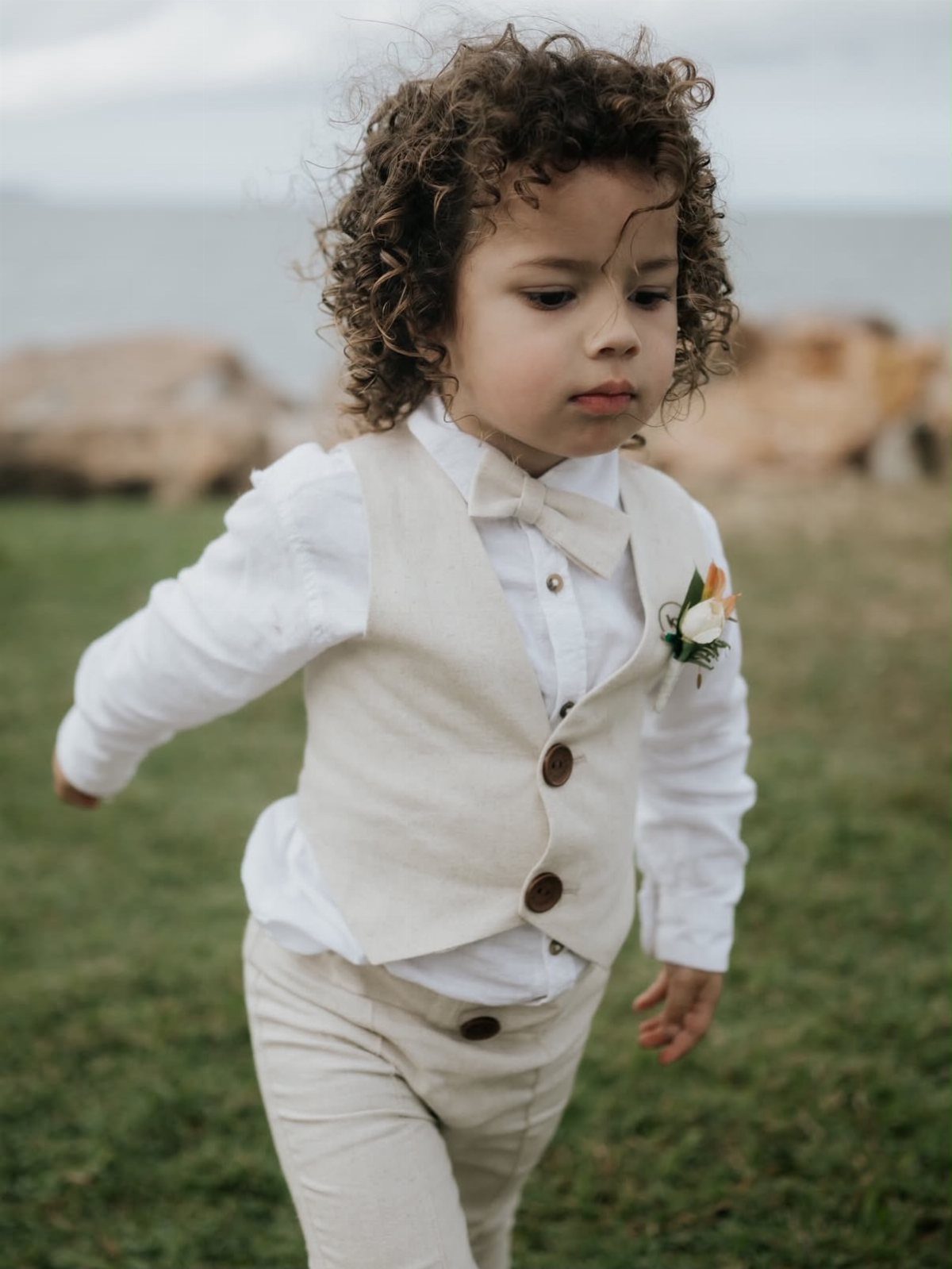 Young boy wearing a beige vest, bow tie, and trousers for a wedding.
