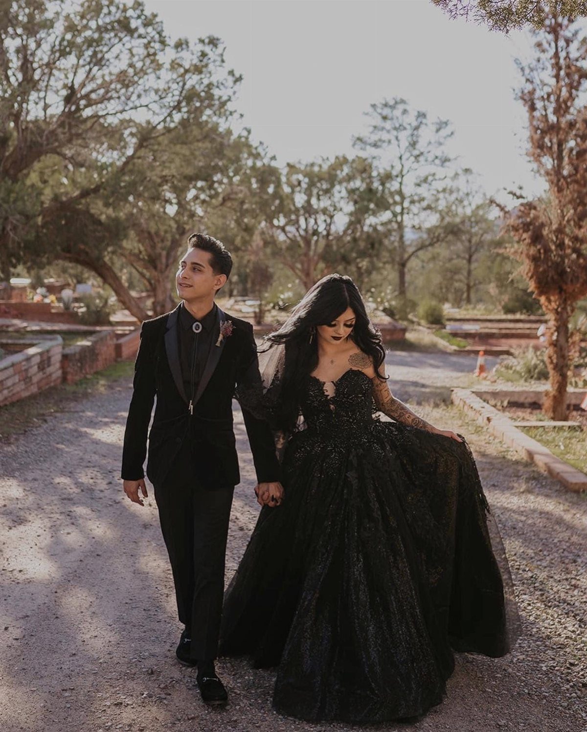 Couple walking outdoors, woman wearing a voluminous black lace wedding gown and man in suit.