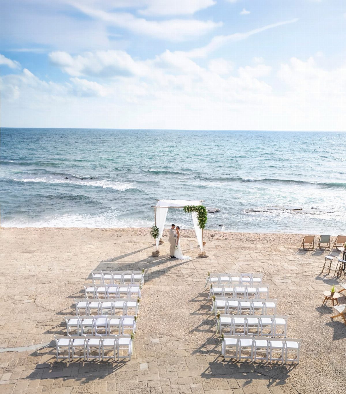 Wedding ceremony setup on a beach with white chairs and a canopy arch.