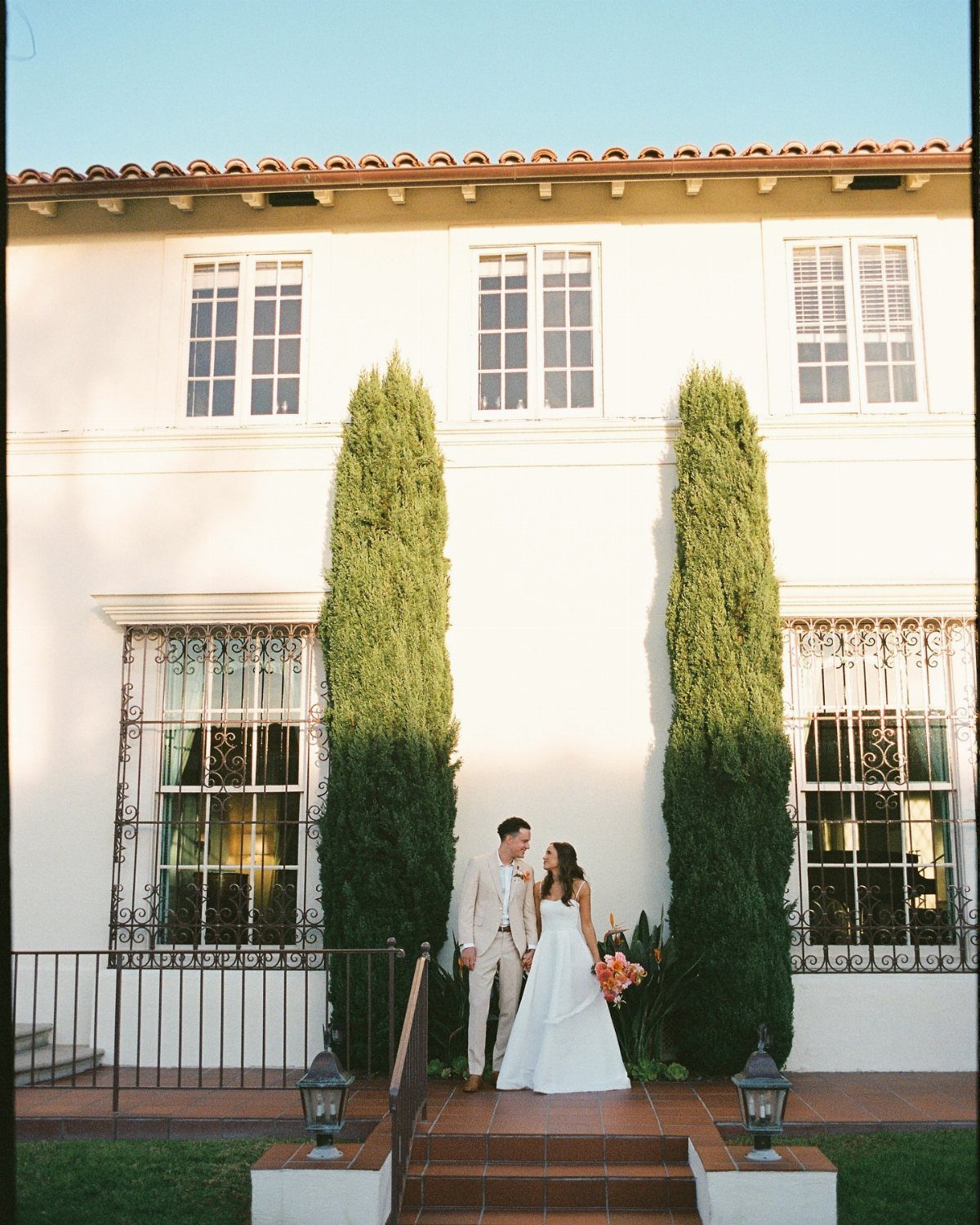 Bride and groom posing in front of a white historic mansion with cypress trees.