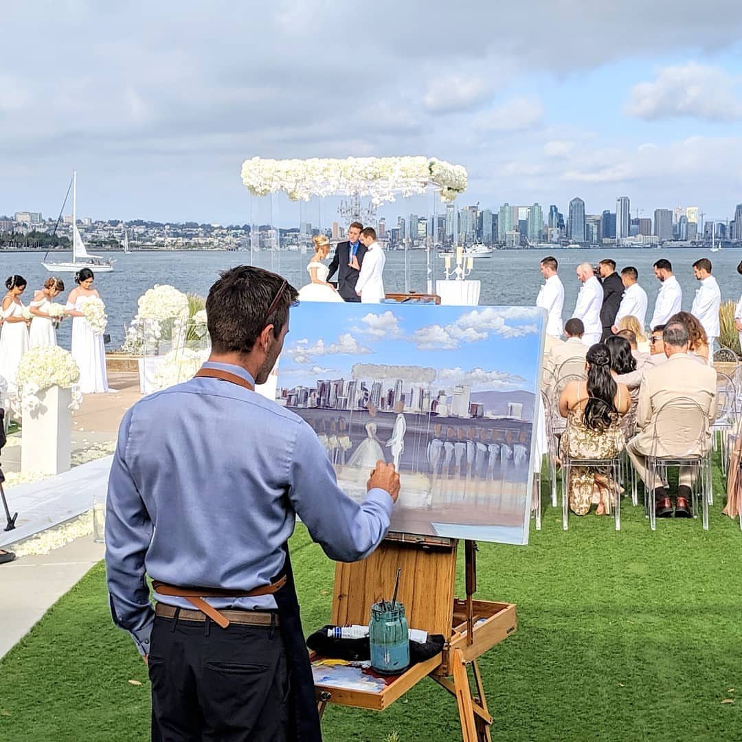 Artist painting a waterfront wedding ceremony with a city skyline in the background