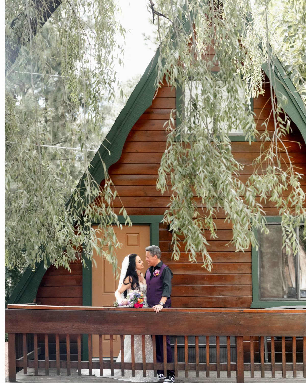 Bride and groom posing on the wooden porch of a rustic log cabin.